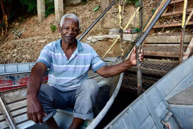 Morador do Cerrado, o pescador Norberto é um homem negro com cabelos grisalhos e olhos escuros. Norberto veste camisa clara listrada e sorri em seu barco.